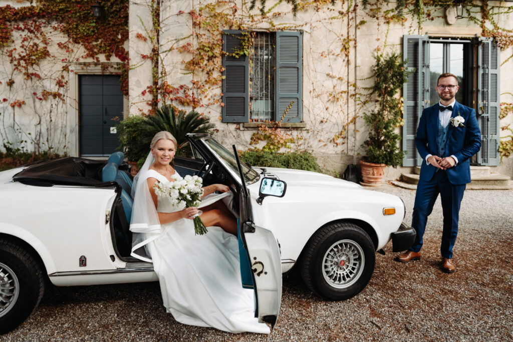 Bride stepping out of a vintage white convertible, holding her wedding dress