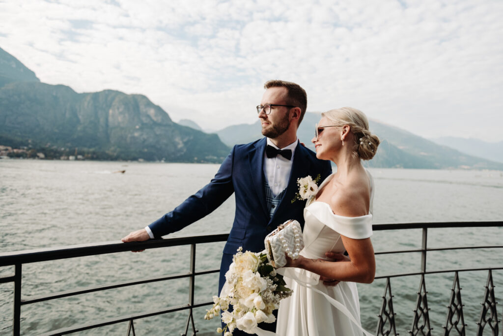 Bride and groom standing by a railing, looking at each other with Lake Como in the background