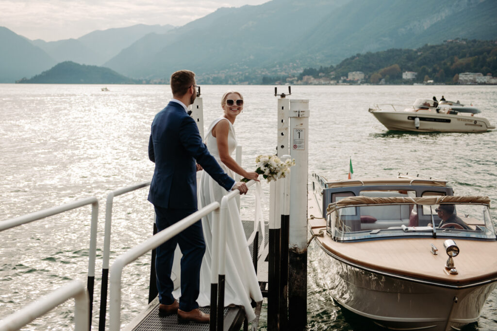 Groom holding the bride’s hand as she steps onto the dock in her wedding dress