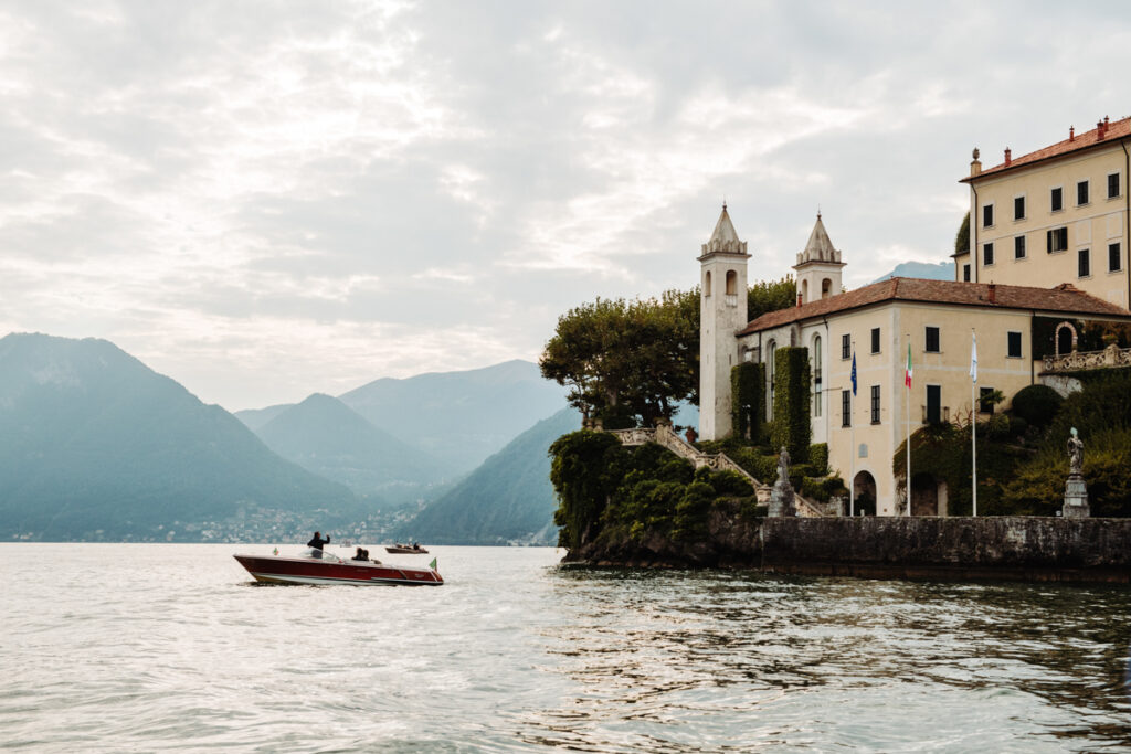 Boat passing in front of Villa del Balbianello, with mountains in the background