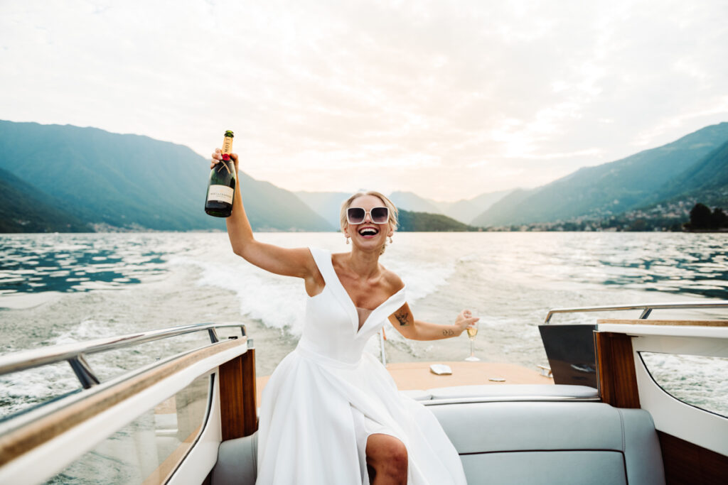 Bride laughing joyfully while holding a champagne bottle on a boat in Lake Como