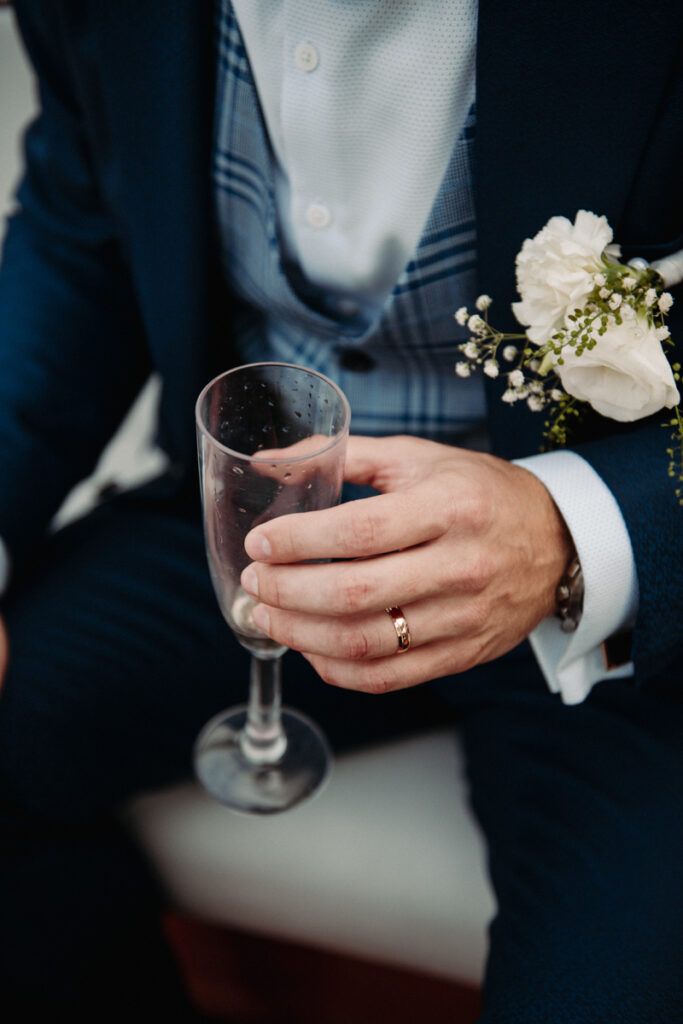 Close-up of the groom’s hand holding a champagne glass, with a white boutonnière on his suit