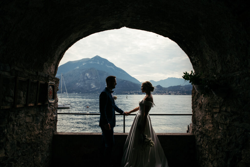 Bride and groom standing under an archway, framed by the mountains and waters of Lake Como