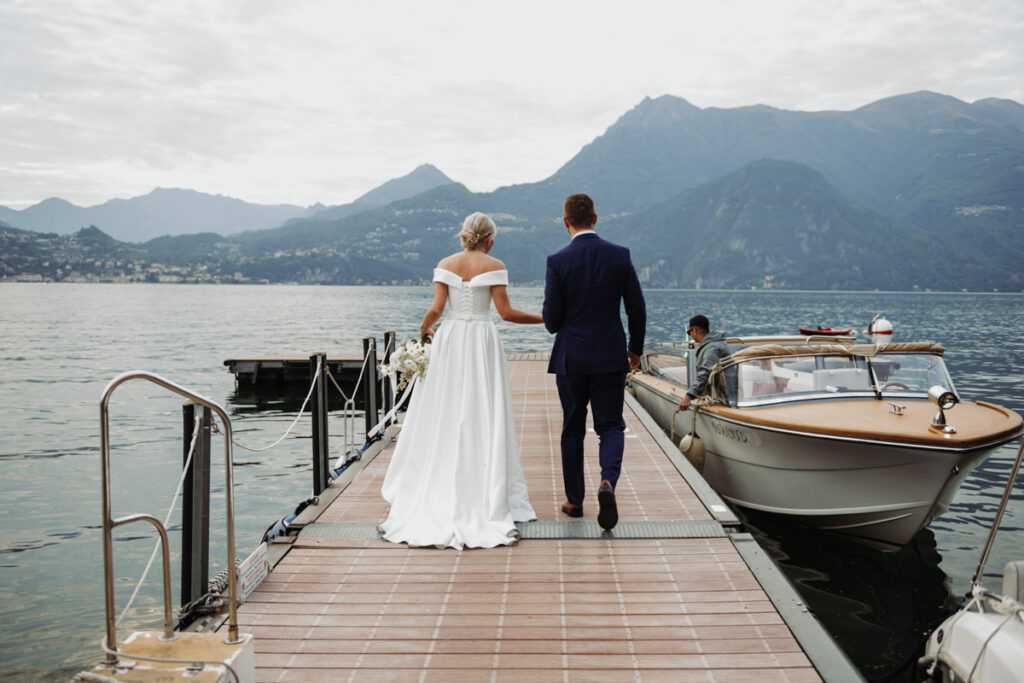 Bride and groom walking hand in hand on a dock with the mountains of Lake Como in the background