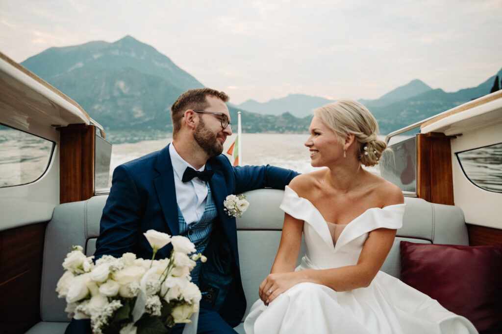 Bride and groom smiling at each other while sitting on a boat, holding the bridal bouquet