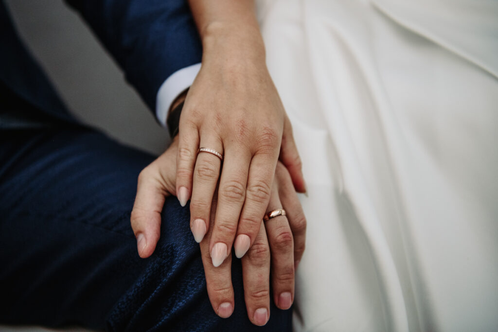 Close-up of the bride’s hand resting gently on the groom’s leg, showing her wedding ring