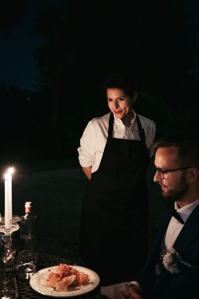 Chef smiling while serving dishes during an outdoor candlelit dinner