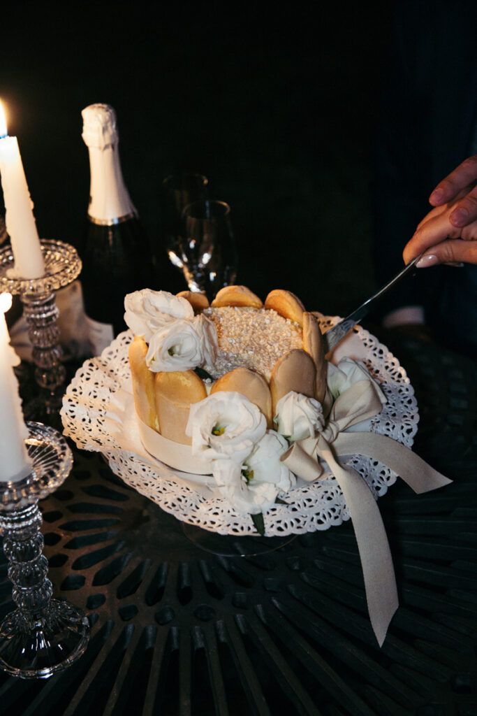 Close-up of hands slicing a cake decorated with white flowers and candles