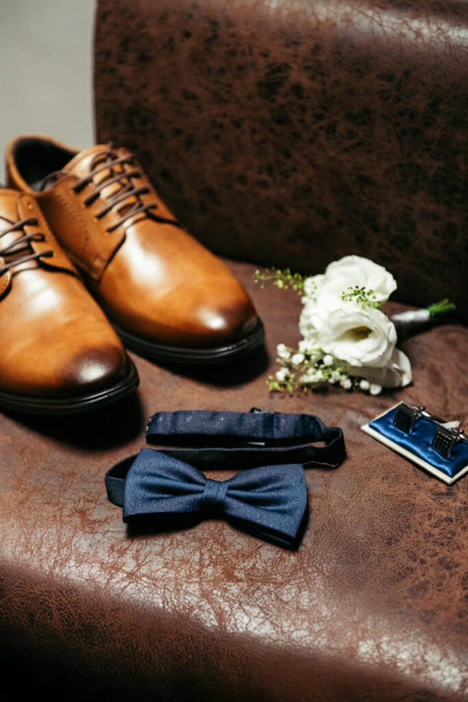 Groom’s shoes, bow tie, and boutonnière neatly arranged for the wedding