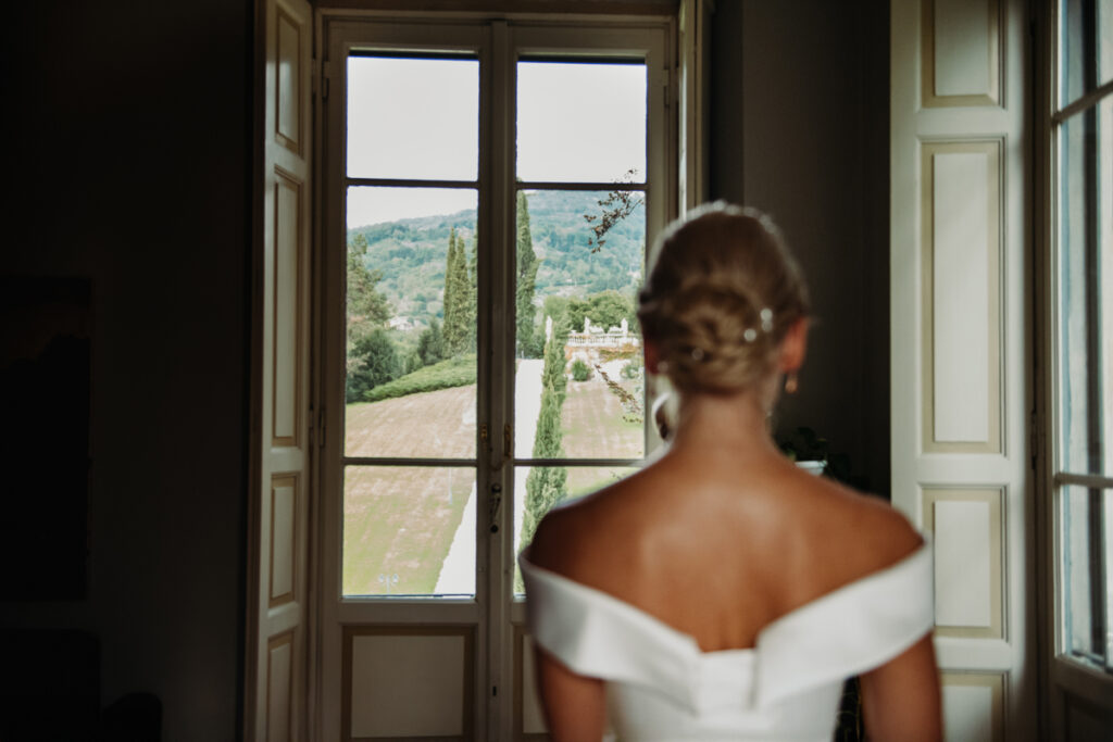 Bride standing by a large window, looking out at the garden