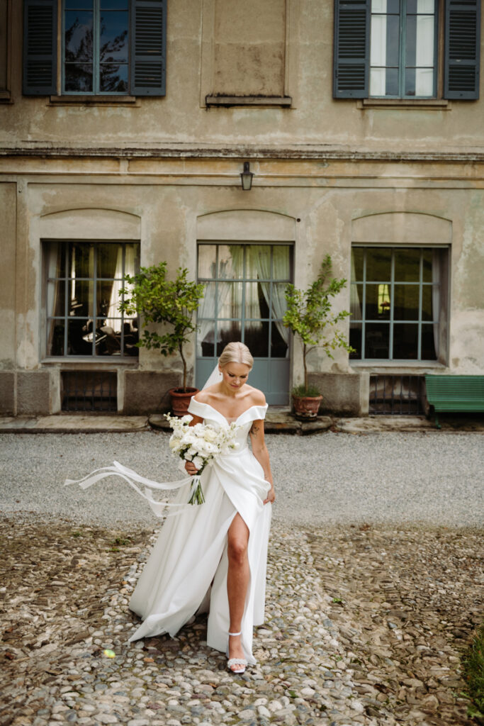 Bride walking confidently in her wedding dress, holding her bouquet outside an Italian villa