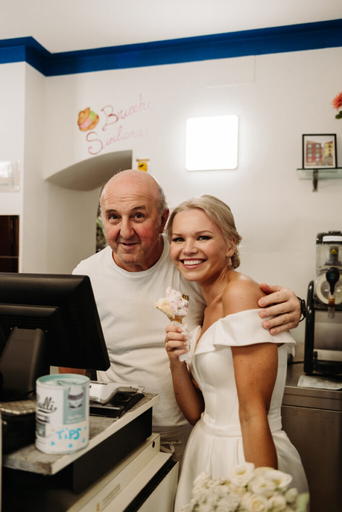 Bride smiling while posing with a local gelato vendor inside a shop