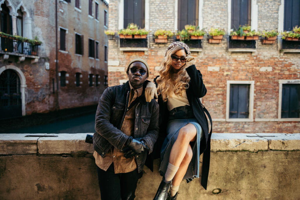 Fashionable couple posing against historic brick buildings in Venice, Italy.