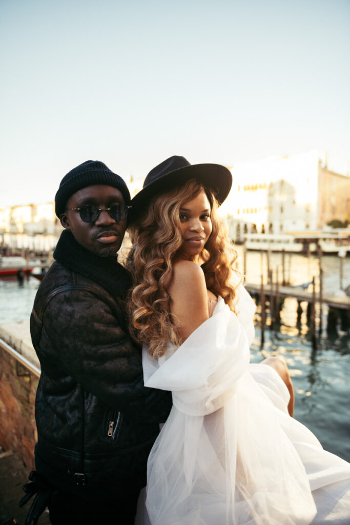 Bride in a stylish hat leaning into her groom, enjoying the Venice golden hour.