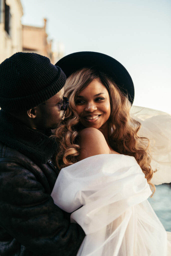 Bride smiling as she leans on her groom, with the Venice waterfront behind them.