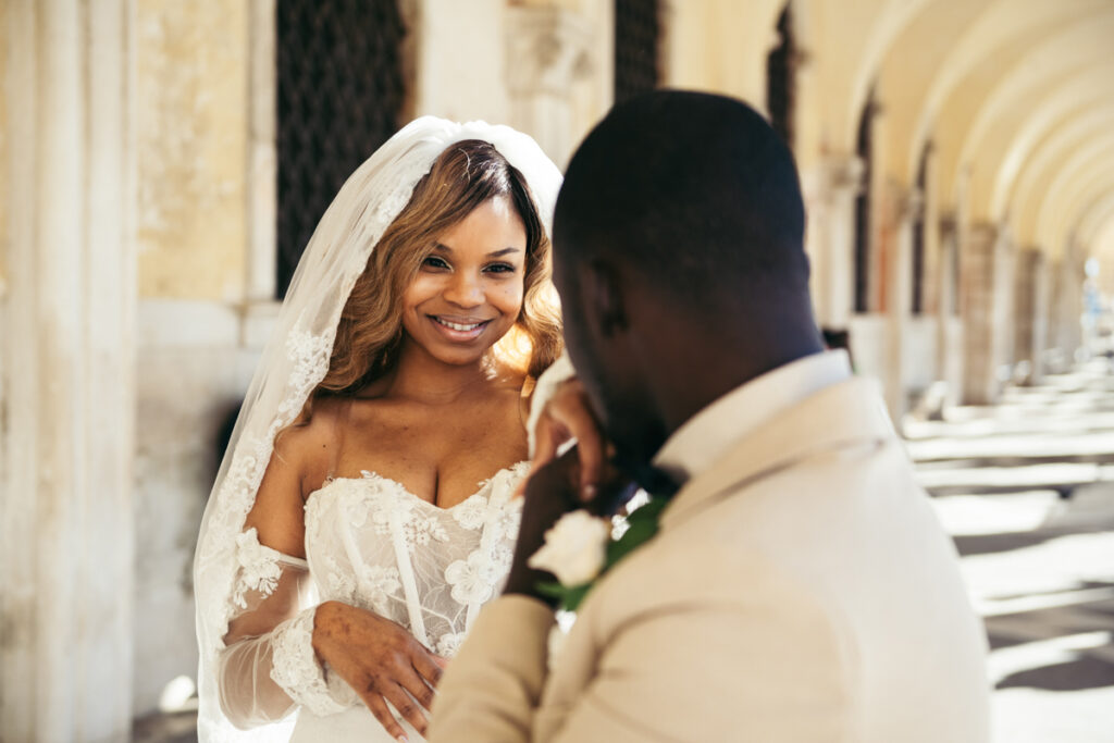 Bride smiling at her groom while he kisses her hand.