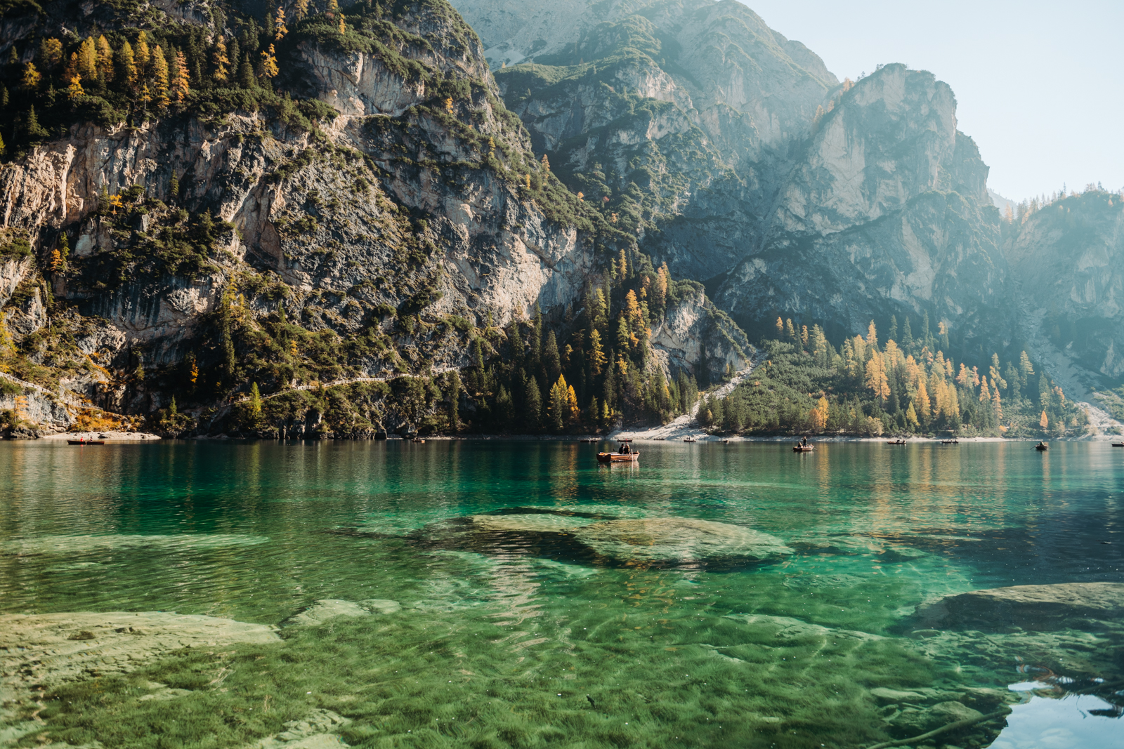 Golden autumn trees lining the shores of Lago di Braies, with mountain peaks in the background.