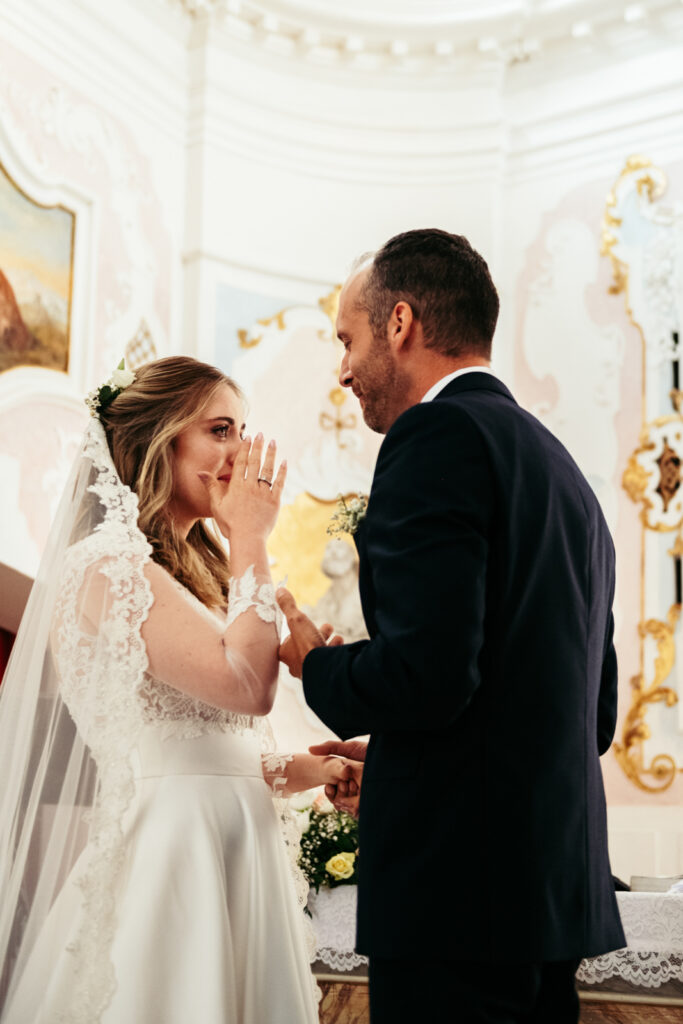 Bride and groom smiling and teary-eyed during the emotional ring exchange.