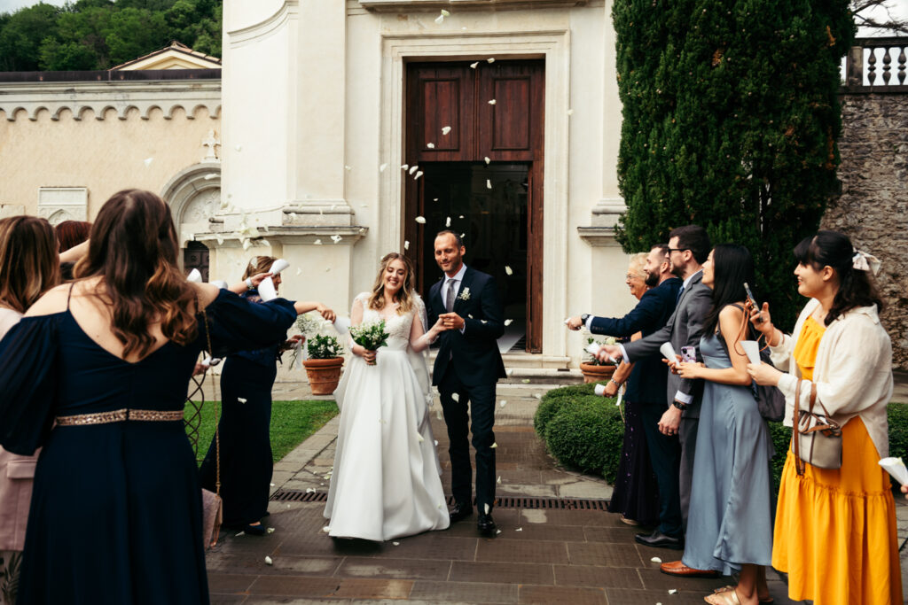 Bride and groom exiting the chapel as guests throw flower petals in celebration.
