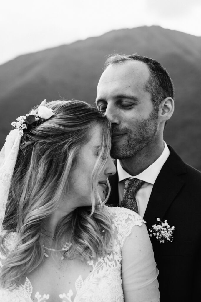 Groom gently kissing the bride’s forehead with a mountain view behind them.