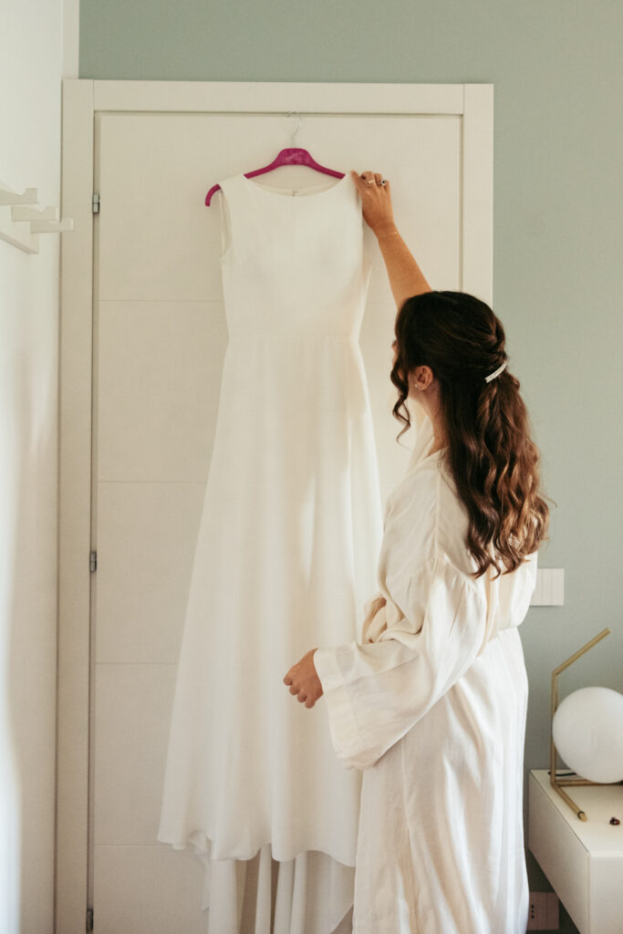Bride admiring her wedding dress hanging in the room before changing