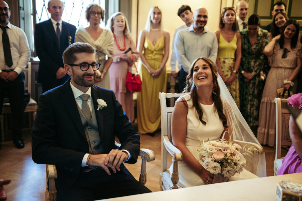 Bride and groom sitting together, surrounded by smiling guests
