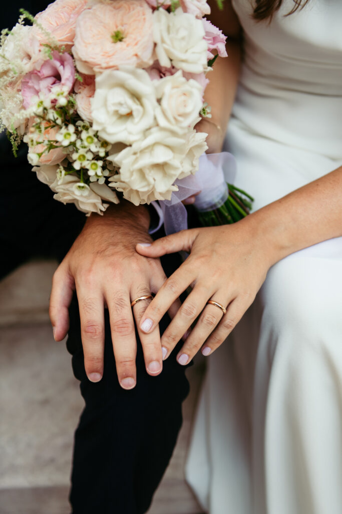 Hands of the bride and groom with wedding rings and bouquet in focus