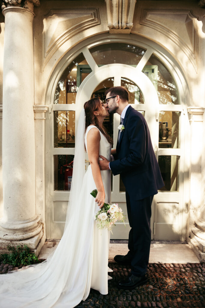 Bride and groom kissing in front of an arched window at Villa Elena in Bergamo