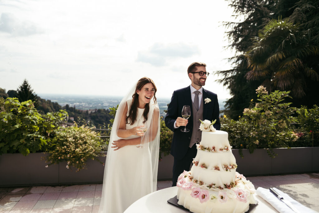 Couple cutting their tiered wedding cake on the villa terrace overlooking Bergamo