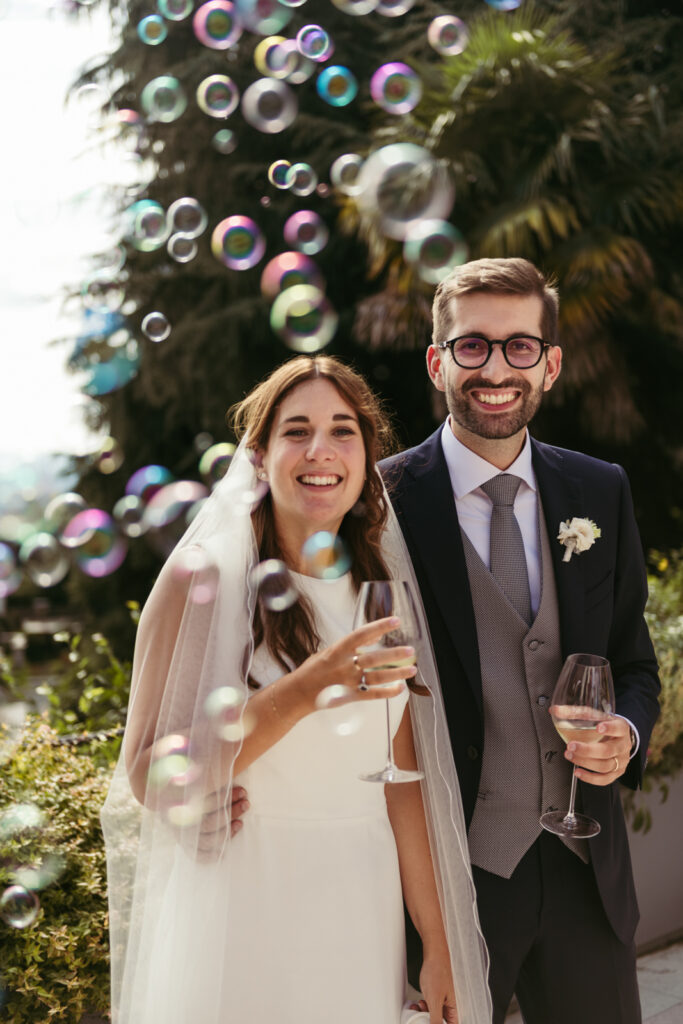 Bride and groom smiling with champagne as bubbles float around them