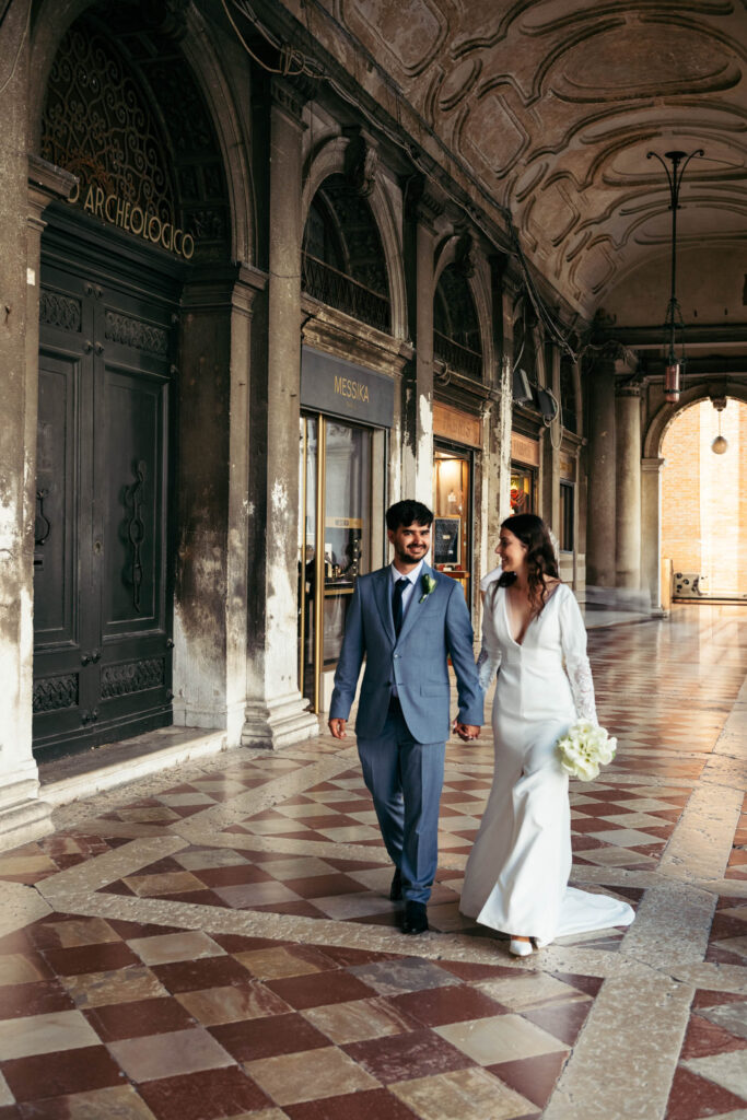 Walking through the colonnades of Piazza San Marco after their symbolic gondola wedding in Venice