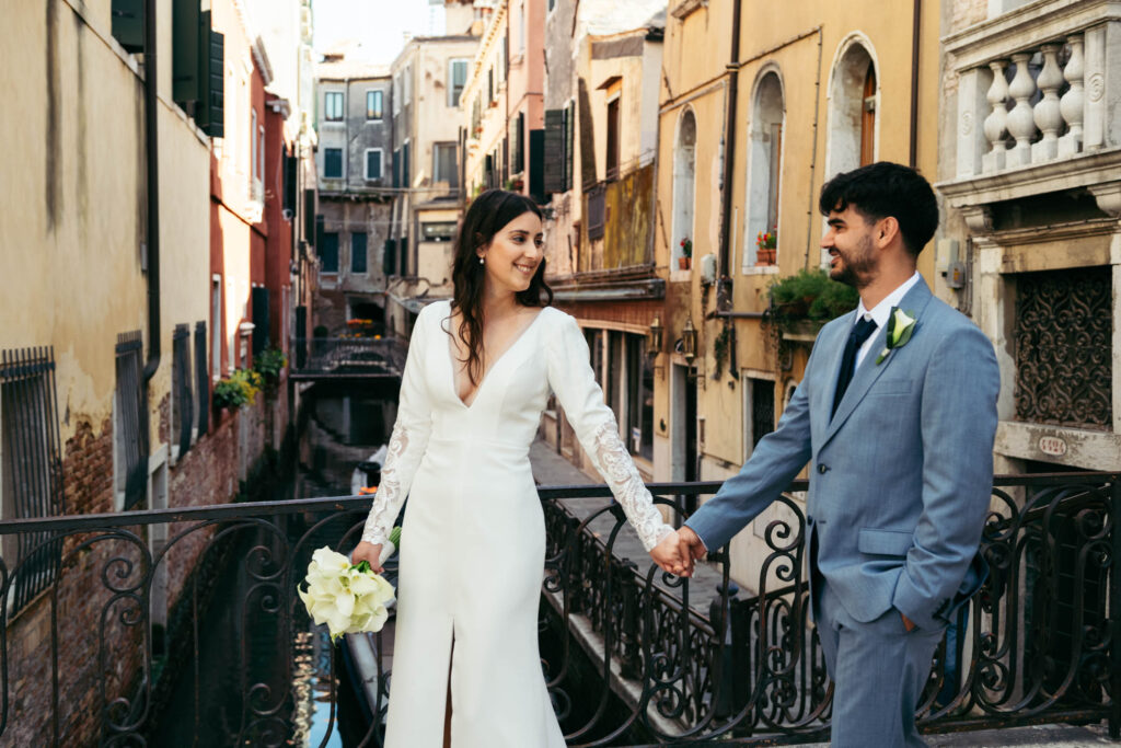 Bride and groom walking hand in hand along a canal during their elopement in Venice