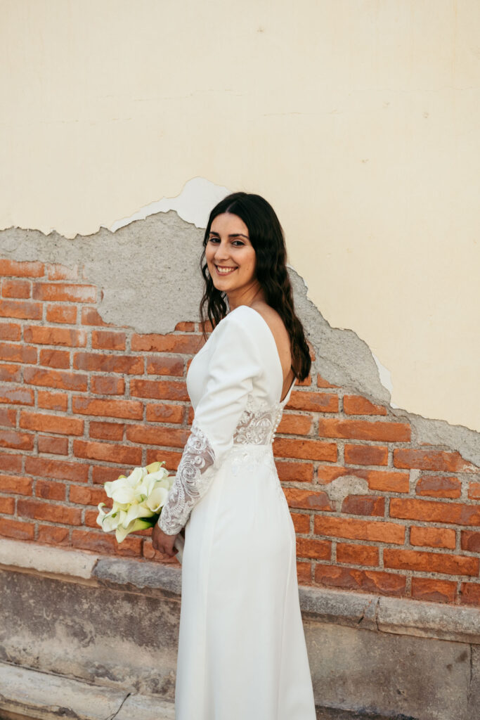 Bride smiling in front of rustic wall with bouquet before symbolic gondola ceremony in Venice