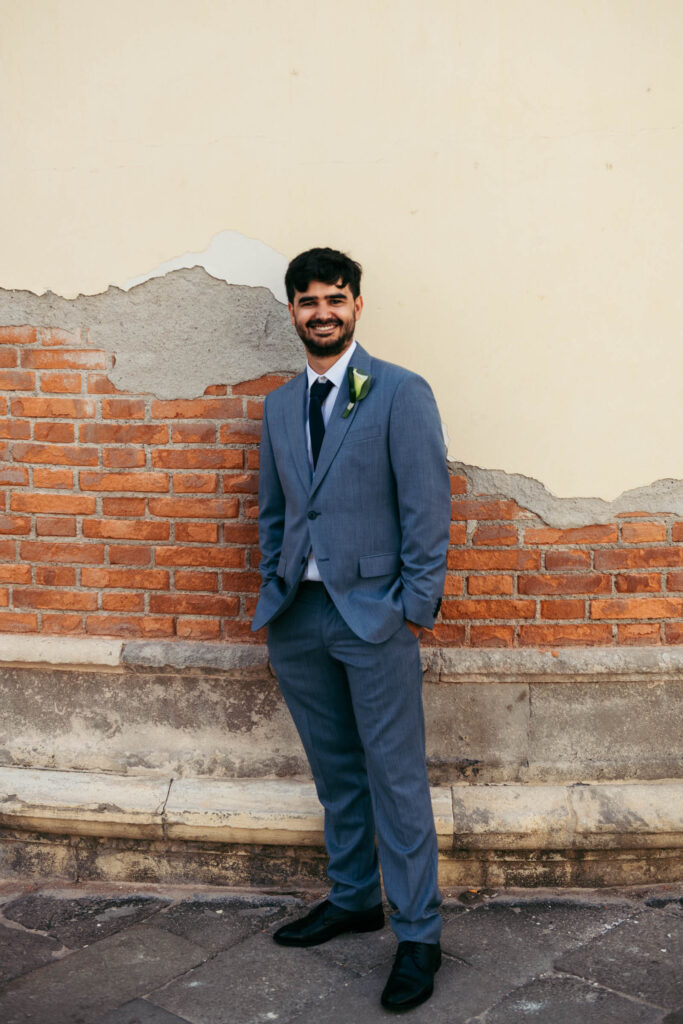 Full-length portrait of the groom smiling in blue suit, captured in Venice before symbolic wedding