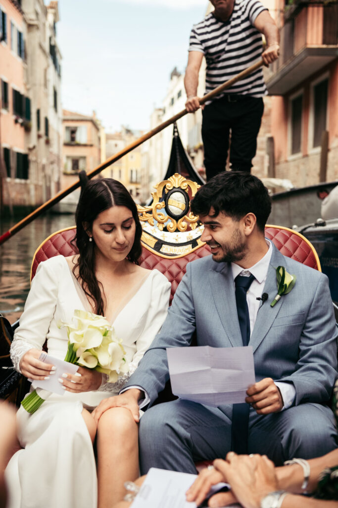 Groom reading his vows while bride listens, holding bouquet on their symbolic gondola ceremony