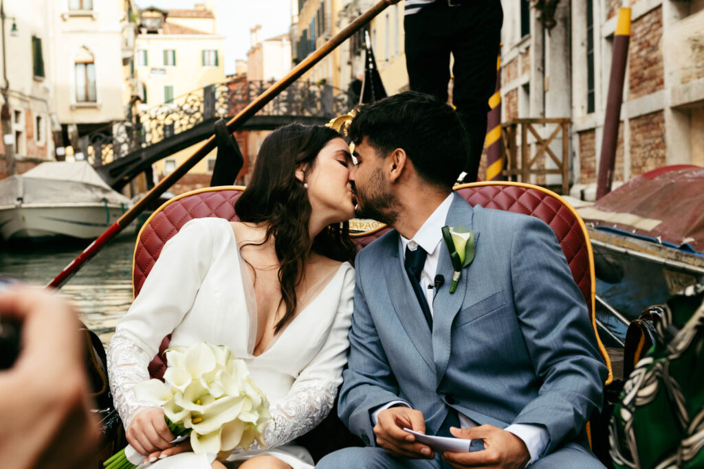 Kiss on a gondola during symbolic wedding in Venice, surrounded by historic canals