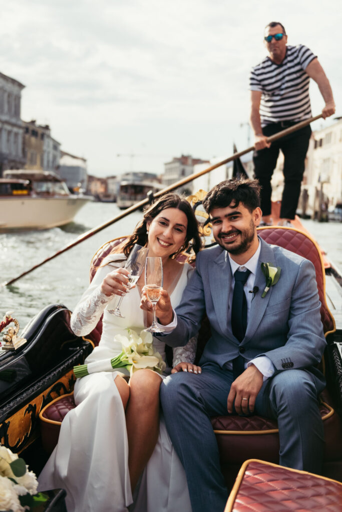 Bride and groom toasting with champagne on a gondola during their symbolic wedding in Venice