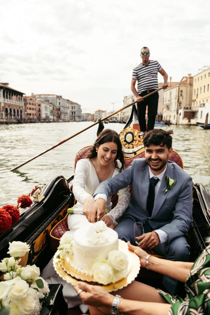 Couple enjoying their symbolic wedding on a gondola in Venice with a floral wedding cake