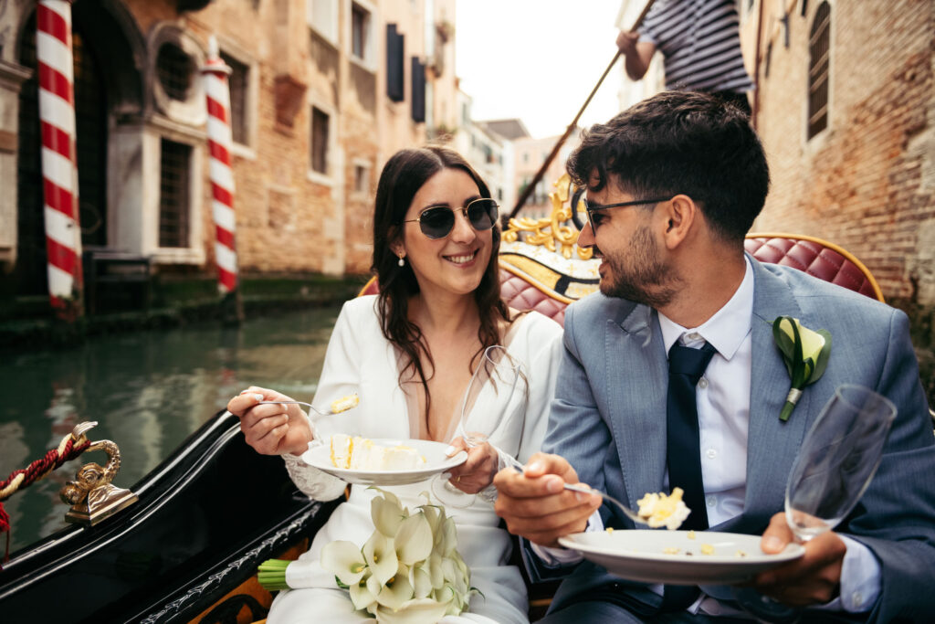 Couple laughing and sharing cake during symbolic gondola wedding in the canals of Venice