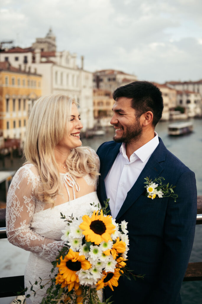 Bride and groom smiling at each other on a bridge over the Grand Canal during their elopement in Venice