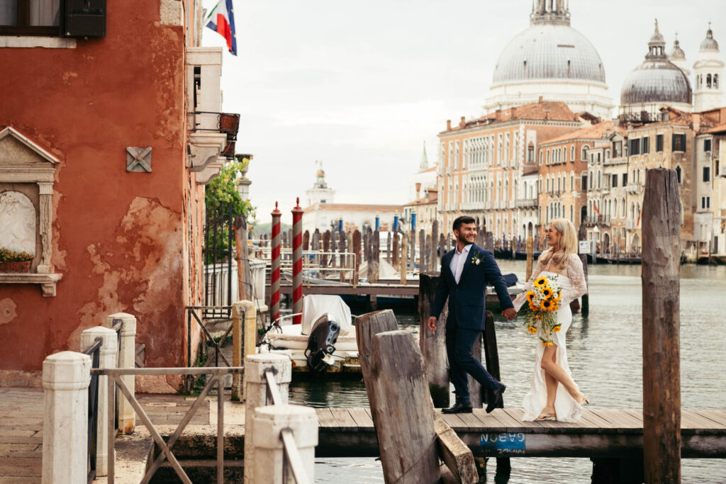 Bride and groom walking on a wooden dock near the canal with Santa Maria della Salute in the background