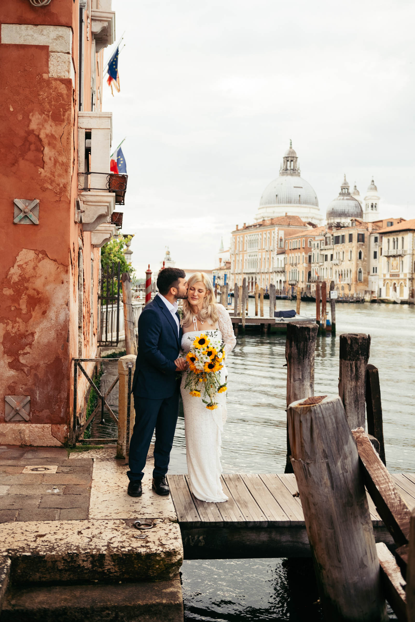 Couple smiling with a sunflower bouquet in front of the Grand Canal during their elopement in Venice