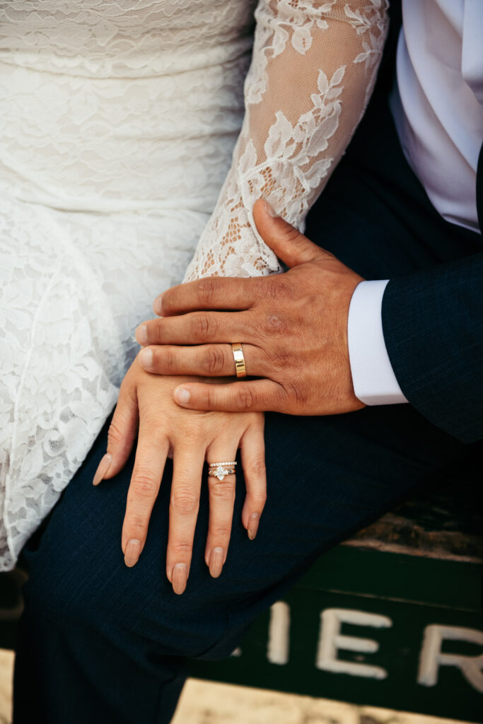Groom holding bride’s hand with visible rings and lace sleeve detail