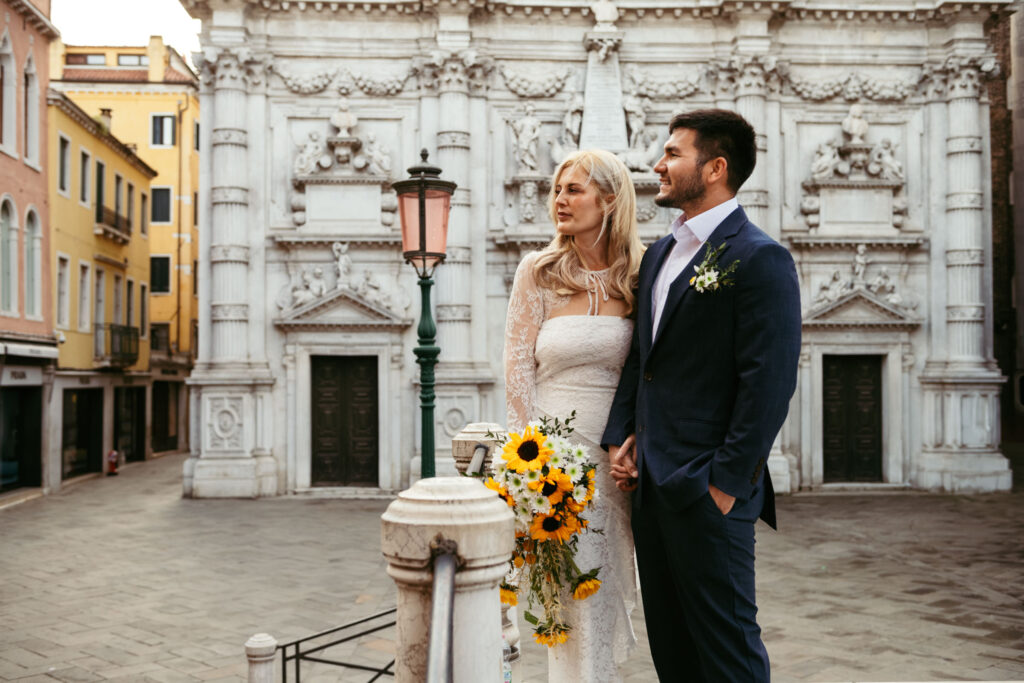 Couple standing together with bouquet in front of white stone church in Venice