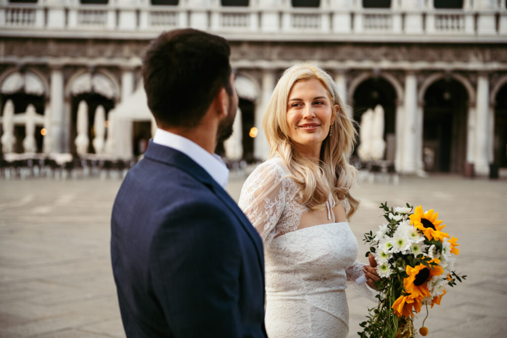 Bride smiling as the groom looks at her, surrounded by Venice architecture