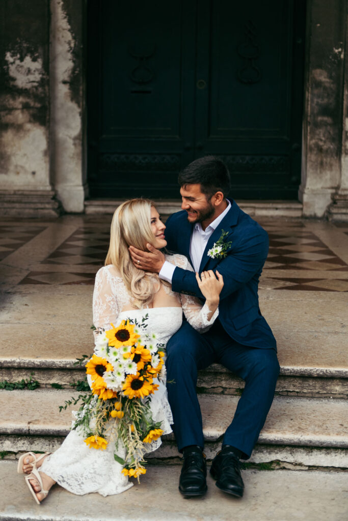 Couple sitting on steps with sunflower bouquet after deciding to elope in Venice
