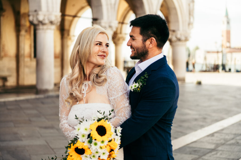 Groom holding bride close in front of the Doge’s Palace arcade at sunrise