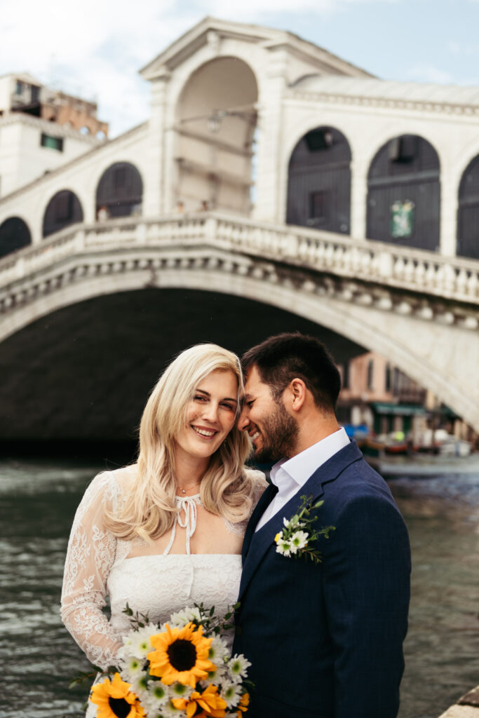 Romantic moment in front of the Rialto Bridge with bride holding a sunflower bouquet