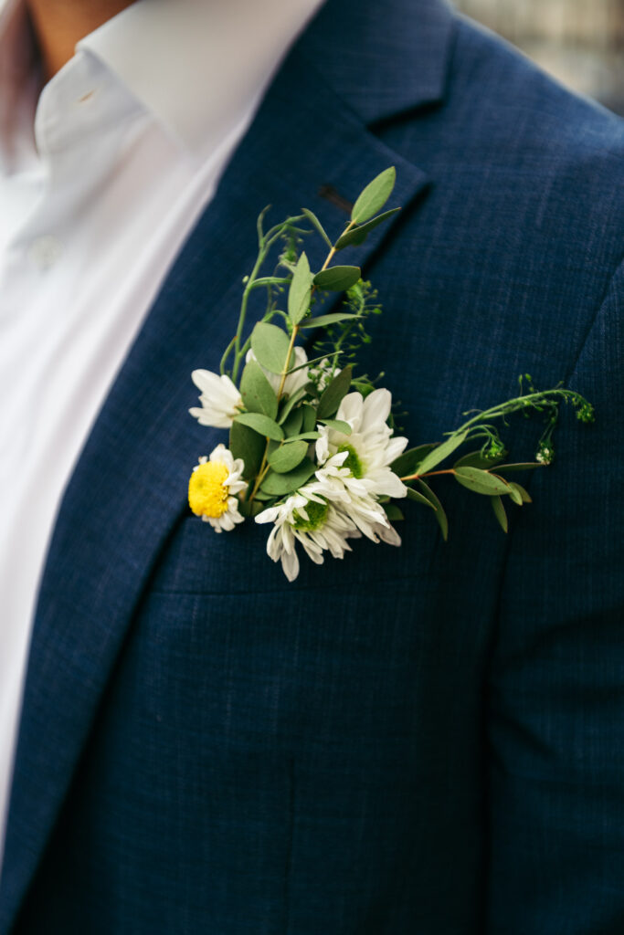 Close-up of groom’s boutonnière with small white flowers and greenery