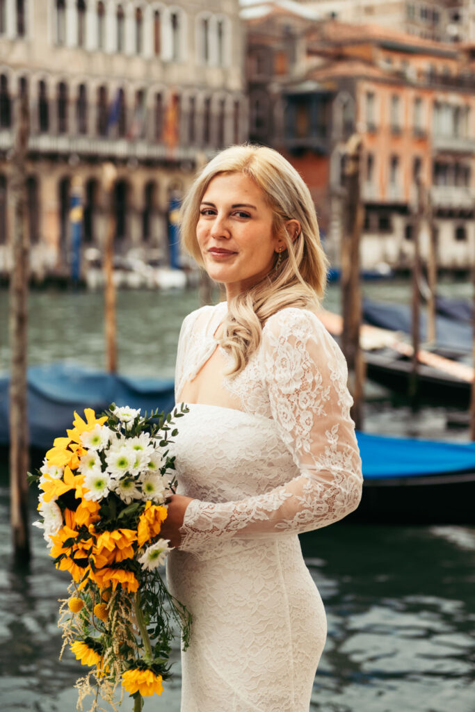 Bride looking away and smiling softly with gondolas behind her during her Venice elopement